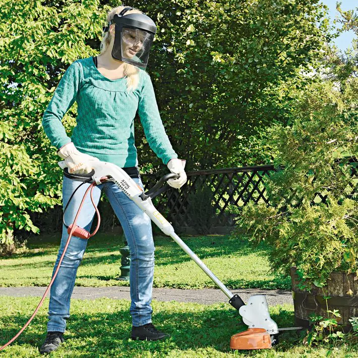 Femme utilisant un coupe-bordures électrique STIHL FSE 52 pour l’entretien du jardin, équipée de gants de protection et d’une visière de sécurité